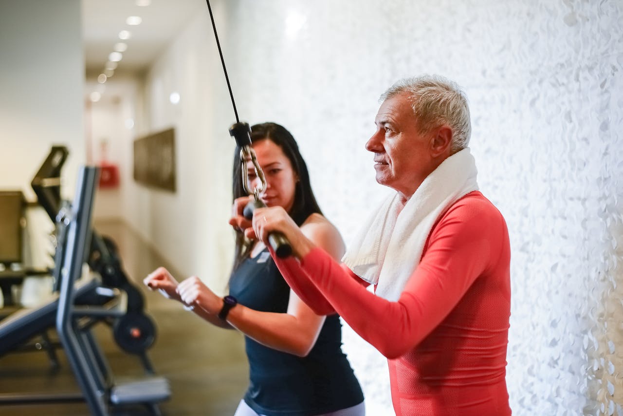 A senior man exercises with a personal trainer in the gym, promoting health and fitness.